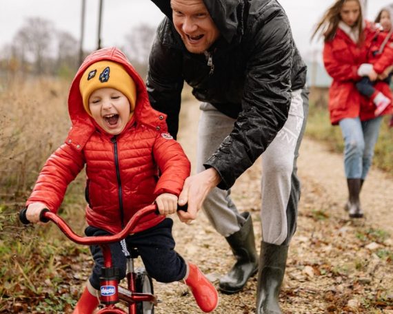 Father helping son ride a bicycle on a fall day while mother and daughter watch.